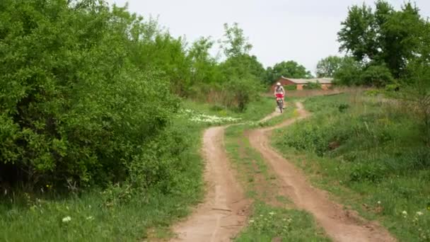 若い男がすぐにパスに沿って緑の春の田園地帯において自転車に乗ります。青少年スポーツ コンセプト — ストック動画