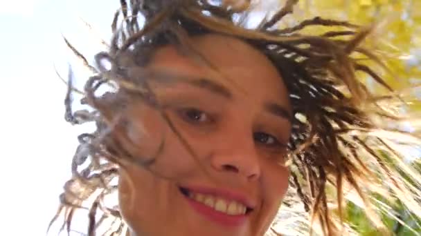 Porträtt av en ung kvinna med dreadlocks. Flickan vrider på huvudet i solen och ler — Stockvideo