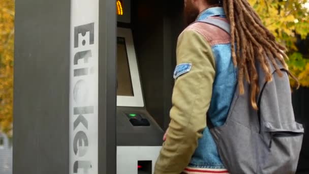 Un turista compra un billete para el transporte público de autobús o metro. Hipster con rastas compra un billete en el terminal electrónico — Vídeos de Stock