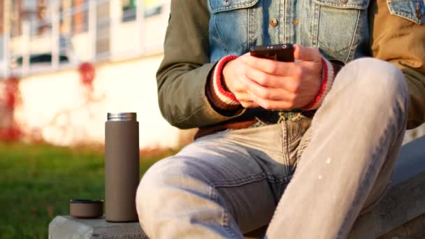 Um homem está a beber chá de uma garrafa térmica na rua. Outono, o conceito de consumo ambiental. Café de casa para o trabalho — Vídeo de Stock
