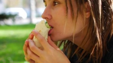 Rastalı genç hippi kız kebap yiyor. Kız parkta fast food shawarma yiyor. Güneşli bir gün.