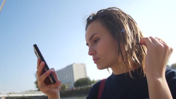 Hipster menina com dreadlocks olha para o telefone. Millennial em redes sociais — Vídeo de Stock