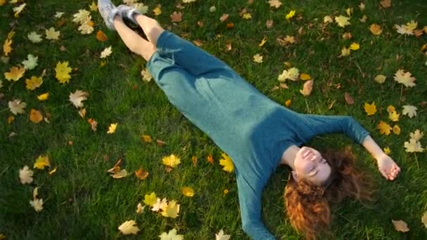 Девушка в платье лежит на зеленой траве с желтыми листьями — стоковое видео