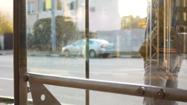 Ein Mann wartet an einer Bushaltestelle auf einen Bus. er kommt zu spät, schaut auf seine Uhr, wechselt von Fuß zu Fuß — Stockvideo