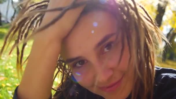 Portrait d'une jeune femme aux dreadlocks. La fille tourne la tête au soleil et sourit — Video