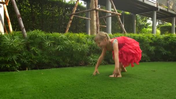 Girl child tumbles sometime on green grass. Child make somersault — ストック動画