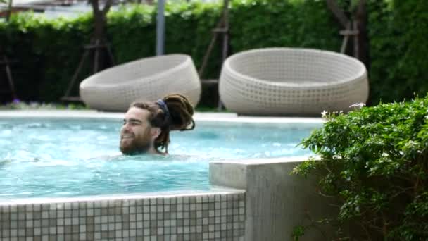 Мужчина плавает в бассейне. Парень с дредами подплывает к краю бассейна и улыбается в камеру. — стоковое видео
