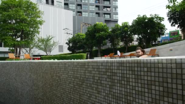 A man swims in the pool. The dreadlock guy swims to the edge of the pool and smiles at the camera — 图库视频影像