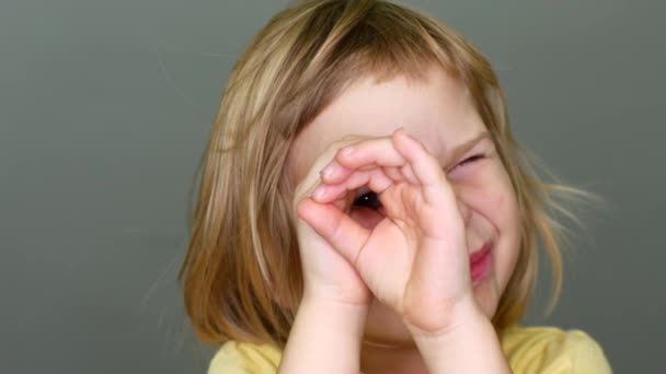 Retrato de uma menina, uma criança faz um telescópio com as mãos e olha para ele. O conceito de aventura e sede de descoberta — Vídeo de Stock