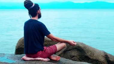 Denize yakın bir taşın üzerinde meditasyon yapan bir adam. Rastalı Lotus Adam.
