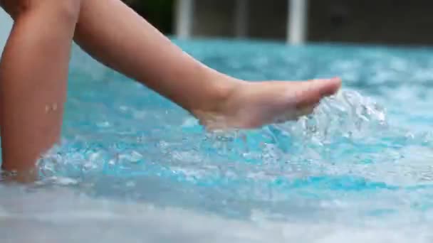 Criança abaixa os pés na piscina. A menina balança na água . — Vídeo de Stock