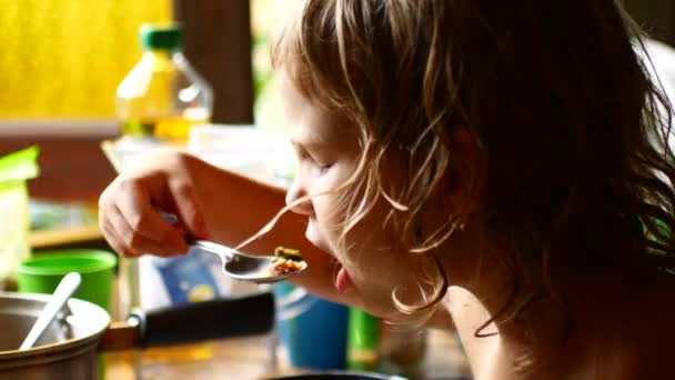 Het kind eet een lepel voedsel uit een pan. — Stockvideo