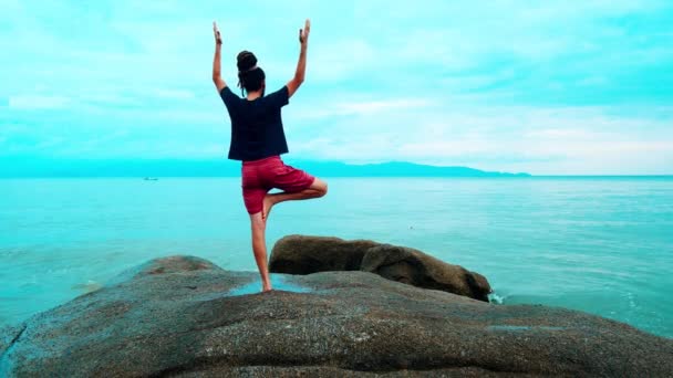Egy férfi jógázik nagy köveken a tenger közelében. — Stock videók