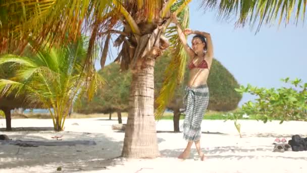 Mooie vrouw aan de kust bij palmbomen. Het meisje zonnebaden in de zon en geniet van de rest. — Stockvideo