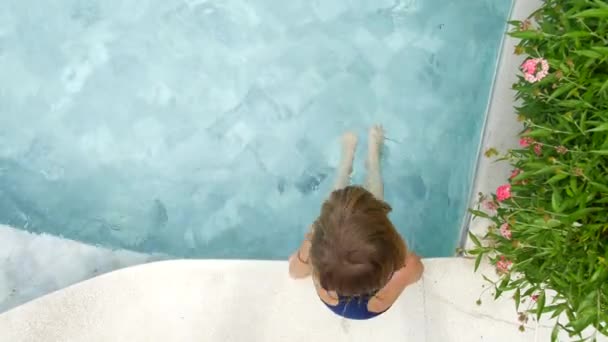 Ребенок сидит на борту бассейна и машет ногами . — стоковое видео