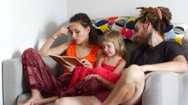 Семья проводит время вместе, женщина читает книгу своему мужу и дочери — стоковое видео