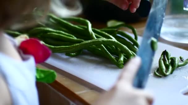 The child helps to cook, cuts a string bean with a knife and transfers it to the pan — 비디오