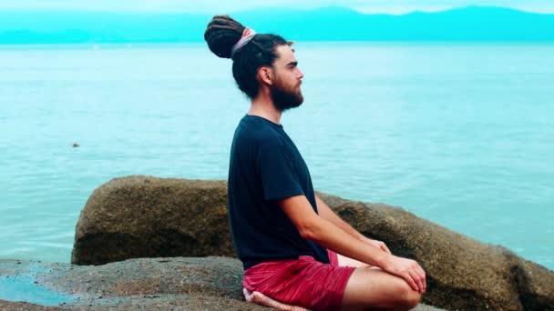 Yogi medita perto do mar. Um homem com dreadlocks na posição de lótus — Vídeo de Stock