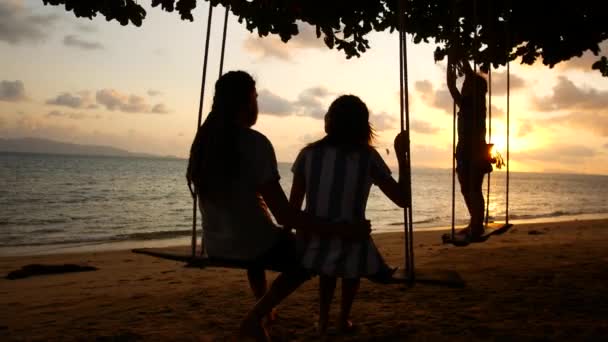 Feliz familia de vacaciones. Mamá papá y bebé paseo en un columpio y ver la puesta de sol cerca del mar — Vídeos de Stock