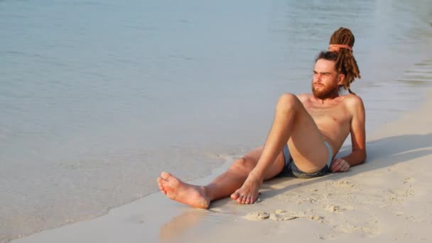 Um homem toma banho de sol em uma praia perto de um mar calmo, um cara gosta do sol e da solidão — Vídeo de Stock