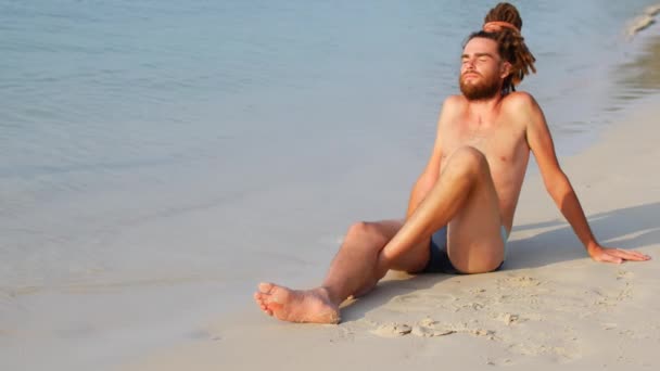 En man som solar på en strand nära ett lugnt hav, en kille njuter av sol och ensamhet — Stockvideo