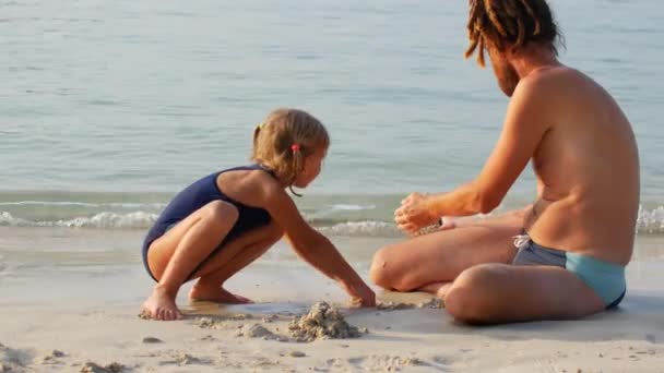 Padre e figlia costruiscono un castello di sabbia sulla spiaggia — Video Stock