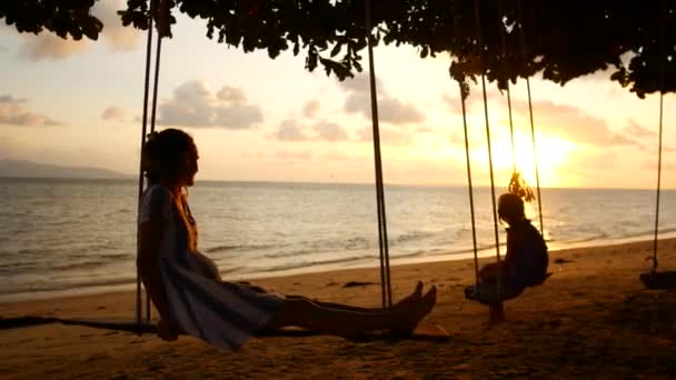 Mor och dotter rida på en gunga vid solig solnedgång nära havet — Stockvideo