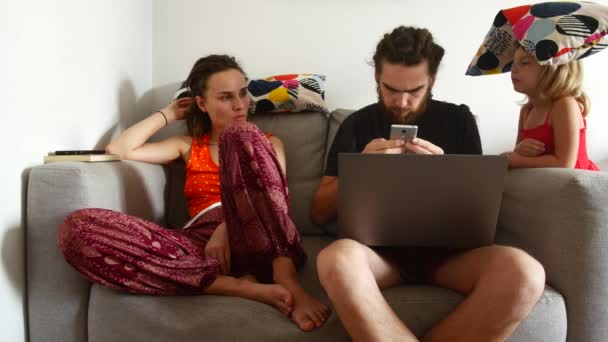 Parents sit on the couch and work, child walks up to dad and distracts adults — 비디오