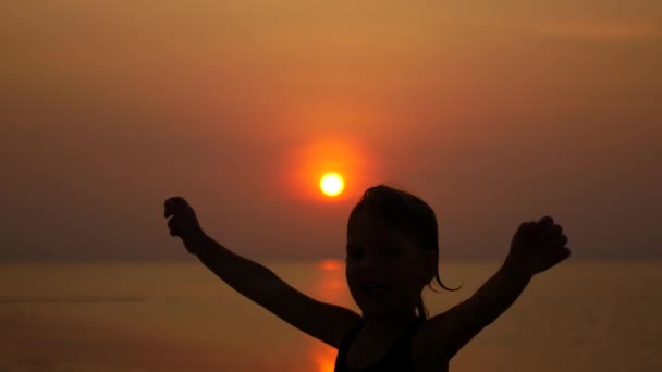 Niña saltando y regocijándose, disparando por la noche en la orilla del mar al atardecer — Vídeos de Stock