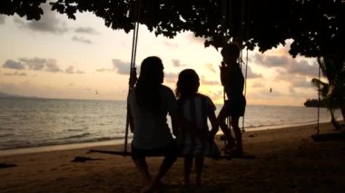 Tatilde mutlu bir aile. Anne ve baba salıncakta sallanıyor ve deniz kenarında gün batımını seyrediyor.