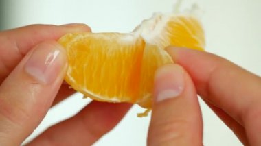Orange is divided into segments by female hands.