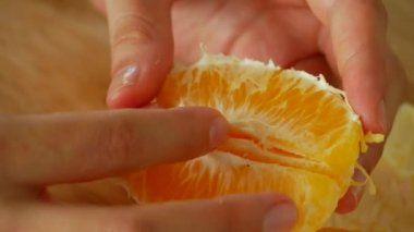 Orange is divided into segments by female hands.