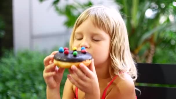 Ребенок ест пончики с шоколадом и сладостями — стоковое видео