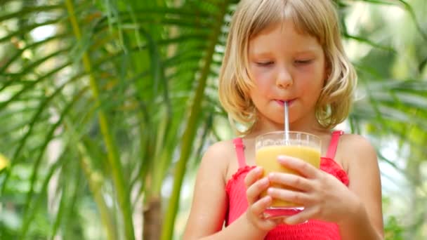 Criança menina bebe smoothie, vídeo em um fundo de árvores tropicais — Vídeo de Stock