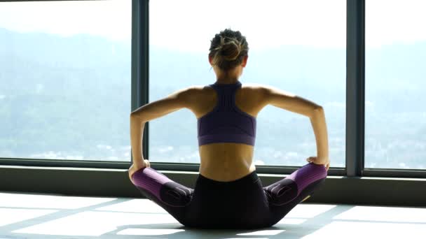 Mujer haciendo estiramiento cerca de una gran ventana en una sala de yoga — Vídeos de Stock