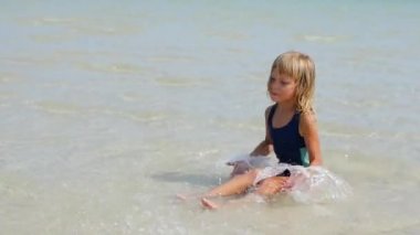 6 yaşında bir kız sığ sularda denizde oturur ve su sıçratır.