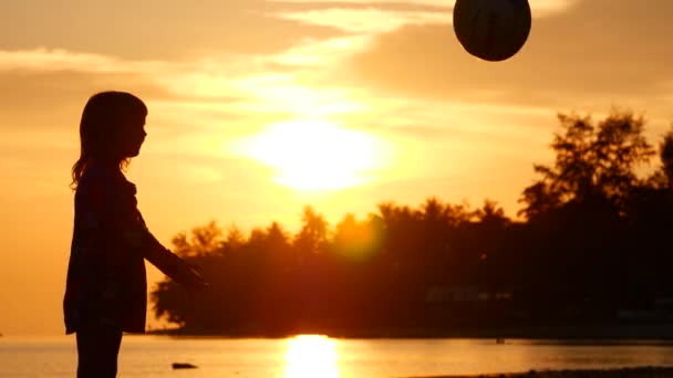 Een meisje speelt bal aan de kust. Silhouet bij zonsondergang — Stockvideo
