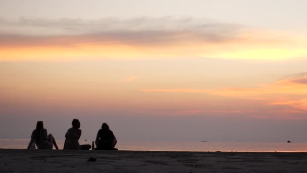 Gün batımında üç kız sahilde oturuyor. — Stok video