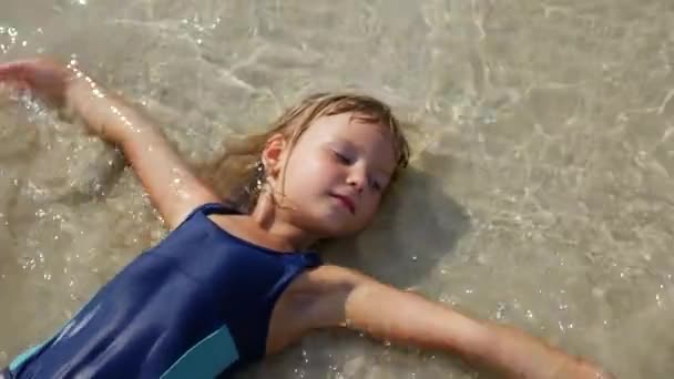 Blond meisje ligt in de zee in ondiep water — Stockvideo