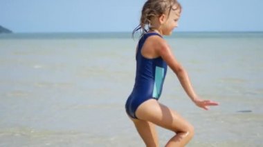 6 yaşında bir kız sığ sularda denizde dans ediyor.