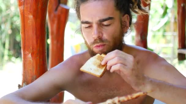 Un joven con rastas y barba come brochetas de pollo — Vídeos de Stock