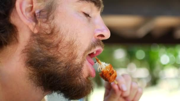 Молодий чоловік з дредлоками і бородою їсть курячих шампурів — стокове відео