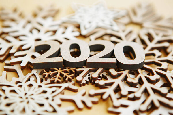 Happy New Year 2020 background with wooden figures and snowflakes made from rustic natural wood material,shot in close up on yellow backdrop