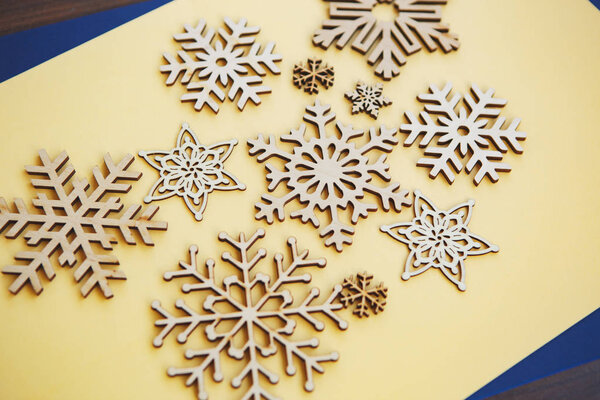 Winter holiday background with handmade wooden snowflakes.Hand made crafts for Christmas and New Year home decor shot from above on yellow background.Beautiful ecological decorative elements for house