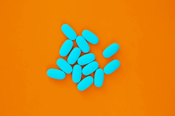 Pile of blue vitamin pills in flat lay on orange background.Prescription medical drugs for illness treatment.Cure disease with pharmaceutical food supplements and vitamins.Medicinal drug for healthy living