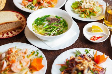 Restorandaki Asya yemekleri. Lezzetli Po Bo çorbası ve deniz ürünleri salataları beyaz tabaklarda servis ediliyor. Sağlıklı beslenmek için doğal malzemelerle lezzetli, egzotik Vietnam mutfağı.