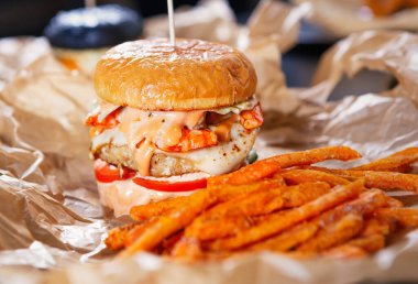 Lezzetli fast food menüleri. El yapımı kahverengi kağıt üzerinde Amerikan fast food. Et pirzolası, yanmış çedar peyniri ve domates ile büyük yağlı çizburger. Teslimat için lezzetli hamburger ve kızarmış havuç çubukları.