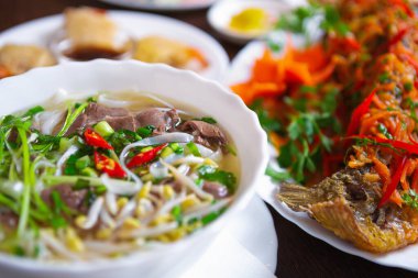 Veitnamese restoranında Pho bo çorbası ve kızarmış balık. Masada egzotik Vietnam mutfağı. Doğal malzemelerle pişirilmiş lezzetli Asya deniz ürünleri. Kırmızı biberli sıcak ve baharatlı biftek çorbası.