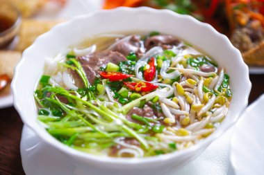Vietnam pho bo çorbası, kırmızı biber ve baharatla karıştırılmış haşlanmış et, fasulye filizi. Geleneksel Vietnam mutfağı menüsünde beyaz kasede servis edilen lezzetli pho çorbası.