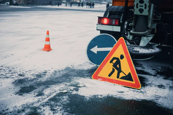 Snowblower clear freezing winter road with snow and ice.Snow-plow remove snow from the city street.Warning road sign and orange cone.Winter service vehicle snow blower work.Careful on snowy icy roads